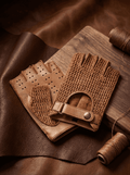 Pair of brown leather gloves on a wooden surface with thread spools.